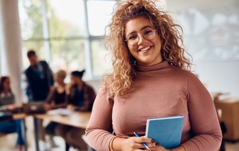 Portrait of happy female student at college classroom looking at camera.